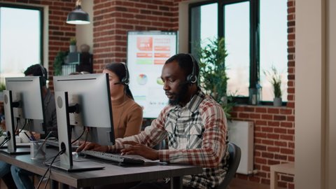 Young man using headphones at call center to help people with telemarketing problems. Helpdesk employee working at customer support service, giving assistance to business clients.