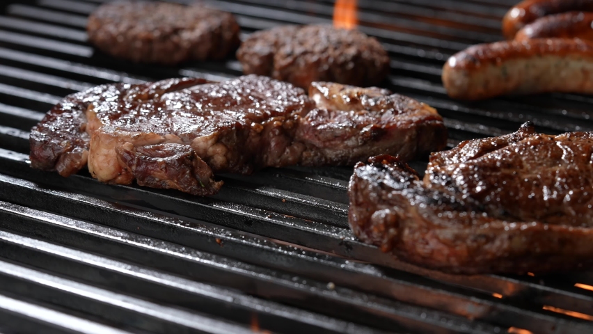 Cooked juicy steak meat beef brushed with rosemary on a flaming grill surrounded by other meat and sausages. slow motion | Shutterstock HD Video #1087811205