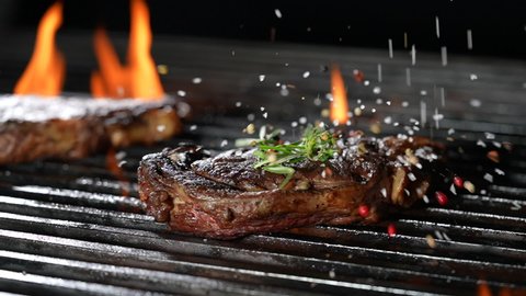 Cooked juicy steak meat beef sprinkled with seasoning on a flaming grill. slow motion