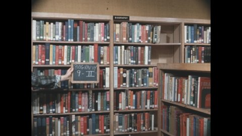 1960s: Hand holding slate. Books on shelves. Woman walking through library, looking at book. Girl putting book on shelf, grabbing another. Person in library.