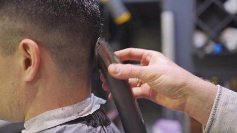 nape. the hairdresser makes a haircut for a brunette man with a hair clipper in a barbershop. professional services. beauty salon for men. cosmetics and products for scalp and hair care.