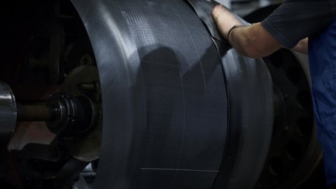 Tyre factory worker hands setting new rubber tape on industrial workshop machine. Close up tire engineering employee working at technological automotive manufacture. Workplace technician job concept