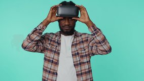 Amazed african american man using headset helmet app to play simulation game. Watching virtual reality 3D 360 video. Young guy in VR goggles isolated on blue background. Addiction from new technology
