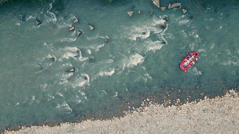 Above view of red inflatable boat drifting through thresholds and stones, rafting on mountain river. Aerial view from drone of group of people rafting in rubber dinghy at daytime. Concept of rafting