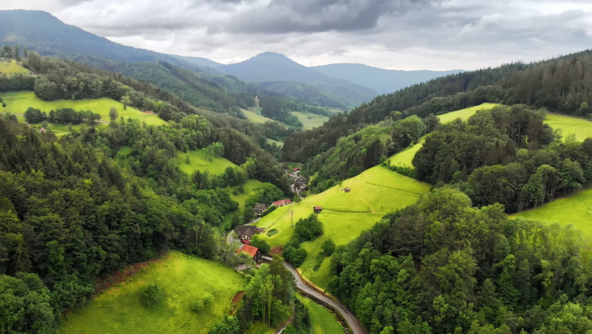 Flight over an idyllic green valley in the Black Forest (Schwarzwald), Germany. With forests, meadows on hills and a few houses in soft light
