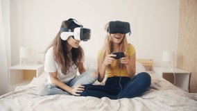 Exited girls in VR helmets at home. Two women in virtual reality headsets sitting on bed, playing video games and having fun together. 3D technology. concept of virtual reality, Gaming, friendship. - Powered by Shutterstock - Get 15% off with code: PIKWIZARD15