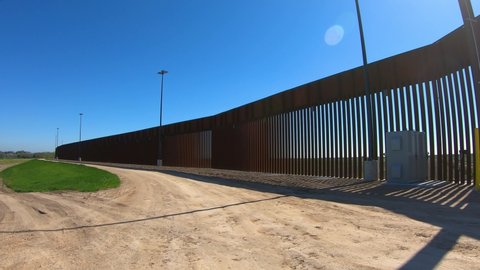 POV driving on Texan gravel service road for the border wall between USA and Mexico; near McCallen Texas on a sunny day; concepts of national defense, border security, and Trump's build the wall