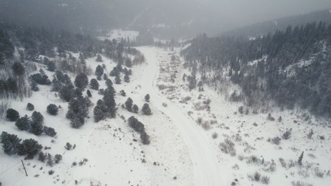 Drone Aerial View of Land Rover Defender D90 SUV Parked on Snow Covered Road in Backcountry Alpine Forest Road in Rocky Mountains near Nederland Boulder Colorado USA During Heavy Snowfall.