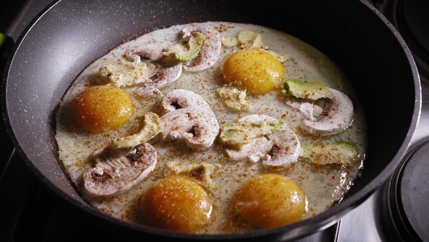Frying Eggs With Mushroom And Avocado In A Skillet, Seasoned With Salt And Pepper. close up