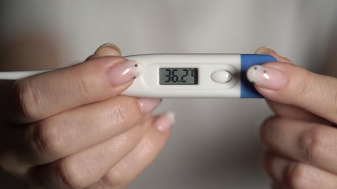 A woman holds a thermometer in her hands to measure body temperature. 36 degrees Celsius. Doctor or nurse, sick patient. Fever from Covid-19 virus. Deadly diagnosis. Coronavirus pandemic, flu epidemic