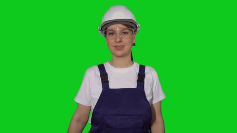 Construction worker. Woman builder in blue overalls and white hard hat hold hand saw. Building, repair and renovation of house or apartment. Female in helmet on green background chroma key.