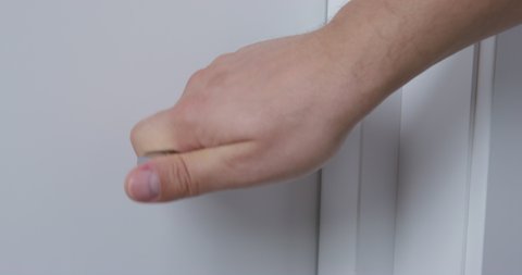 Young man hand pushes silver-colored metallic handle and closes glossy white room door of hotel at good illumination extreme closeup