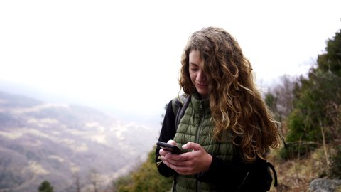 Young caucasian blonde woman chatting with her new smartphone device, posting photo on social media while walking in remote countryside, 5g wireless unlimited data for travel