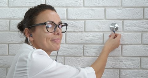 Cute doctor by wall. A cute female doctor puts a stethoscope by the wall in the room.