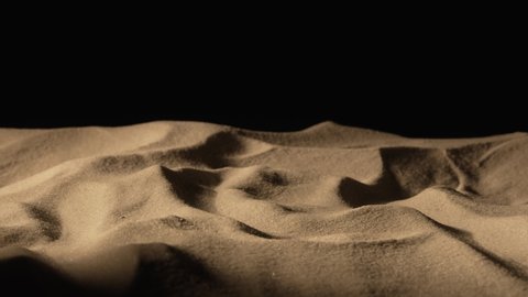 Camera pans over mound of dry sand in dark on black background. Close up shot of sandy dune with grainy particles sparkling in the light. Slow motion ready, 4K at 59.97fps.