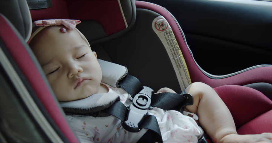Close up - cute Asian baby girl sleeping and dreaming in a car seat in vehicle back seat. Happy family road trip. Child’s passenger care and safety product concept.  Royalty-Free Stock Footage #1087840107