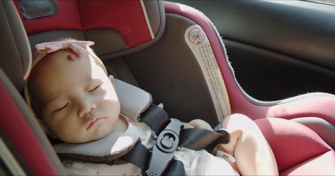 Close up - cute Asian baby girl sleeping and dreaming in a car seat in vehicle back seat. Happy family road trip. Child’s passenger care and safety product concept. 