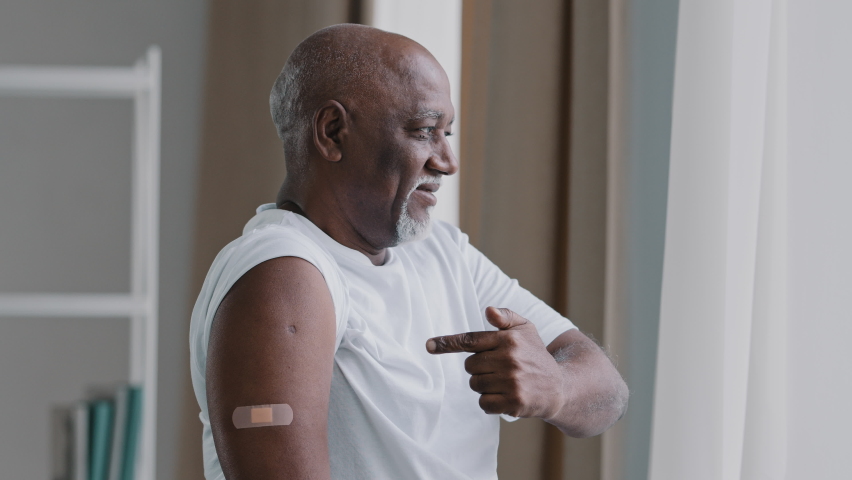 Happy elderly african american man show adhesive bandage on shoulder after vaccination smiling grandpa looking at camera satisfied immunization point finger at medical patch disease protection concept Royalty-Free Stock Footage #1087841761