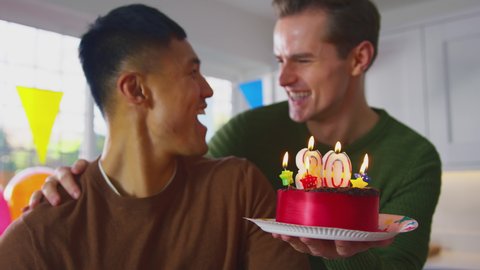 Same sex male couple celebrating 30th birthday at home with surprise cake and candles which are blown out- shot in slow motion