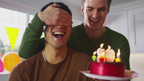 Same sex male couple celebrating 30th birthday at home with surprise cake and presents - shot in slow motion