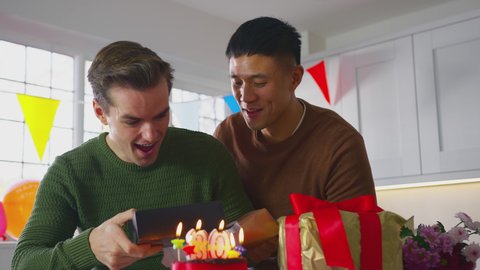 Same sex male couple celebrating 30th birthday at home with man receiving gift from partner - shot in slow motion