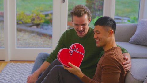 Man surprising partner at home with heart shaped gift held behind his back celebrating birthday, anniversary or valentine's day - shot in slow motion
