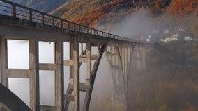 Aerial video of the magnificent Djurdjevica Bridge over the Tara river canyon in the northern part of Montenegro. Beautiful morning fog moves through the arches of the bridge. Shot in the fall season