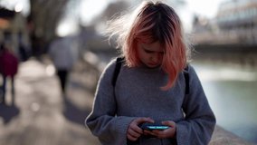 troubled kid on city street, preteen girl with pink hair and smartphone is looking at camera