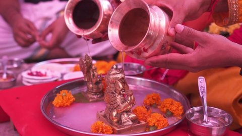 Ganesh puja in Hinduism, man and women pouring holy water on hindu god lord ganesha murty to worship. Indian Wedding Rituals | Selective focused