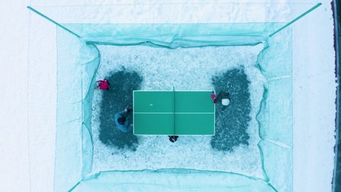 Two people play table tennis on the winter sports ground in the city park. The view from the drone is vertically down.
