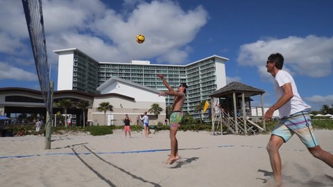 Deerfield Beach, Florida  USA - February 26 2022:  Guys play volleyball in slow-motion in the sand beneath the net in the late-morning sun with condominiums in the background.