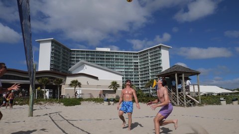 Deerfield Beach, Florida  USA - February 26 2022:  Guys play volleyball in slow-motion in the sand beneath the net in the late-morning sun with condominiums in the background.