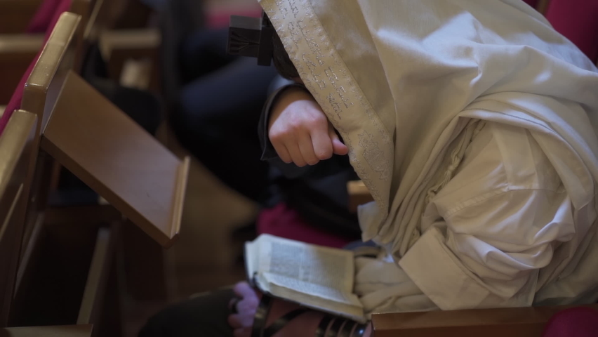 An adult man, a Jew, reads a book while closing his eyes. Prayer, tefillin, tallit,