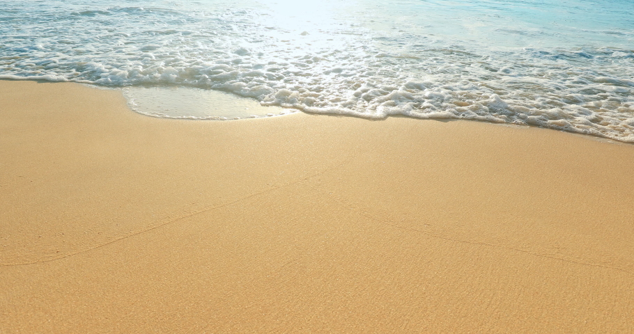 Clean sand beach and soft waves of tropical sea with sun reflection