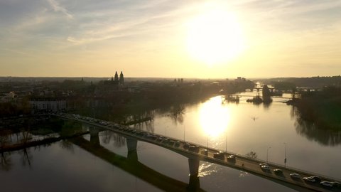 France, Tours city, drone aerial view during sunset (or sunrise) above Loire river with traffic jams on Mirabeau bridge, Saint-Gatien cathedral in the background. Big gold sun and orange sky.