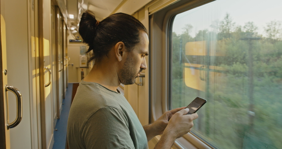 Young tourist with a smartphone looks out of the window of a moving train