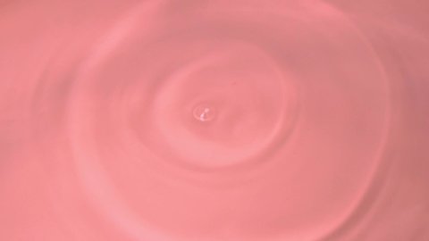 Drops Drip in Coral Pink Water Forming Circles on Water, Close up, Top View, Slow Motion. Coral Pink Abstract Background.