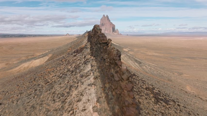 Unique deserted landscape around Ship Rock, New Mexico as seen from above. Drone footage of the stone dunes, stretching towards the rock formation under blue sky. High quality 4k footage