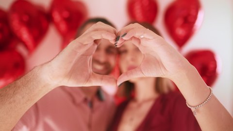 Close up portrait happy young couple faces looking through fingers making heart shape. Real love concept, Valentines Day celebration, romantic relationships, just married spouses, sincere feelings