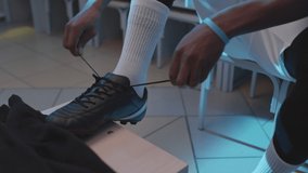 Tilting up of young African American male athlete sitting in locker room, tying up laces on cleats early in morning - Powered by Shutterstock - Get 15% off with code: PIKWIZARD15