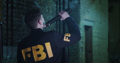 An FBI agent is conducting an investigation at night in the city. A man examines the crime scene, illuminating the dark corners with a flashlight.