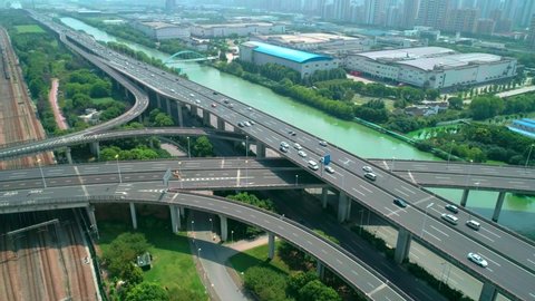 Aerial view of a highway overpass multilevel junction with fast moving cars surrounded by green trees and with a river on a side on a sunny day.