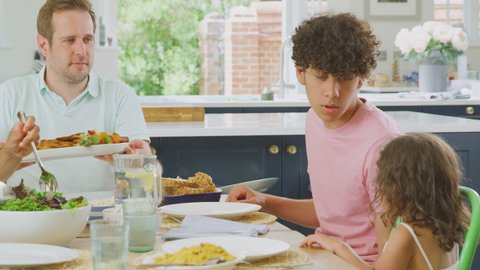 Multi-racial family sitting around table in kitchen at home eating healthy meal together - shot in slow motion