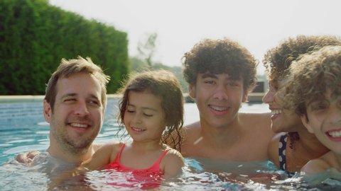 Camera tracks along faces of multi-racial family relaxing in swimming pool on summer vacation together - shot in slow motion