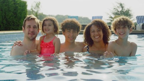 Portrait of multi-racial family relaxing in swimming pool on summer vacation together - shot in slow motion