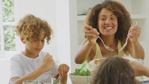 Mother serving as multi-racial family sitting around table in kitchen at home eating meal together - shot in slow motion