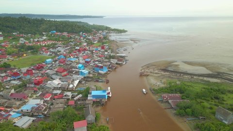 Indonesia, West Sumatra. Drone flying forward above rivermouth and Muara Siberut town on Siberut island in Mentawai, showing houses and boats.