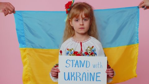 LVIV, UKRAINE - Feb 24, 2022: Toddler Ukrainian girl kid in embroidery dress protesting war conflict raises inscription massage text Stand With Ukraine. Peace, no war, stop Russian aggression