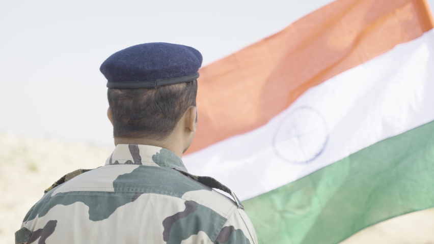 back view shot of Proud Indian army soldier saluting by looking indian flag - concept of patriotic, nationalism and honour