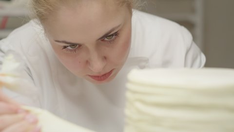 Close up pf chef decorating rotating cake using pastry bag with cream. Bakery process in slow motion.